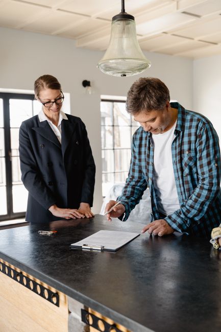 A businesswoman guides a homeowner through property signing at a kitchen counter.