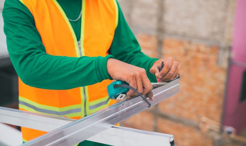 A construction worker measuring a metal frame while wearing a reflective vest, indicating attention to detail.