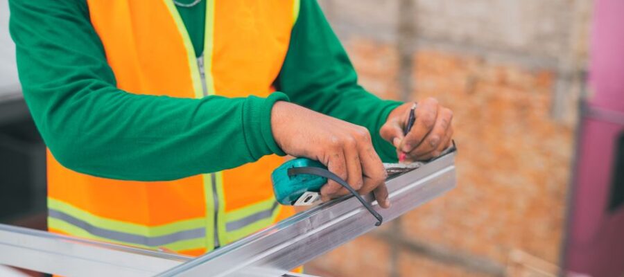 A construction worker measuring a metal frame while wearing a reflective vest, indicating attention to detail.