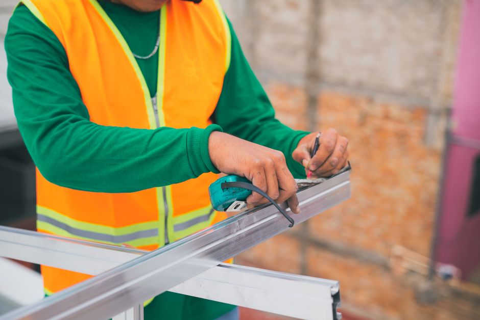 A construction worker measuring a metal frame while wearing a reflective vest, indicating attention to detail.