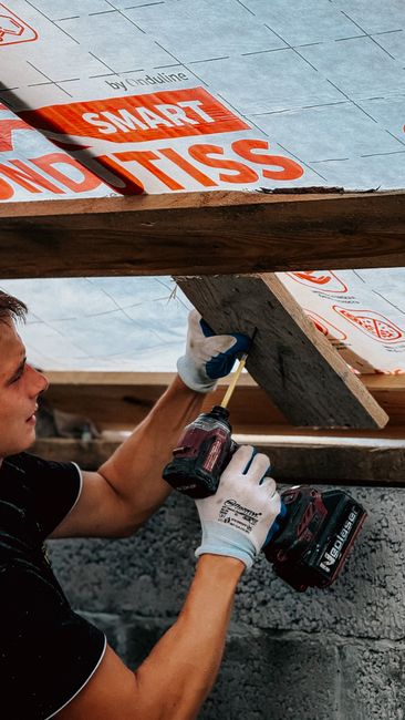 A construction worker uses a drill to install roof insulation, ensuring efficient energy management.