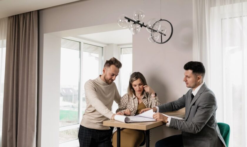 A couple consults with a real estate agent in a modern indoor setting, reviewing property documents.