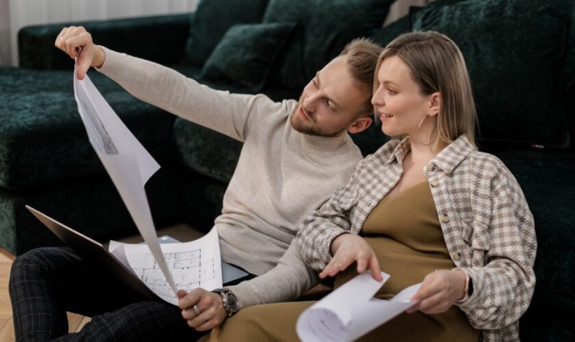 A couple sitting on a sofa reviewing architectural blueprints, symbolizing home buying or renovation.