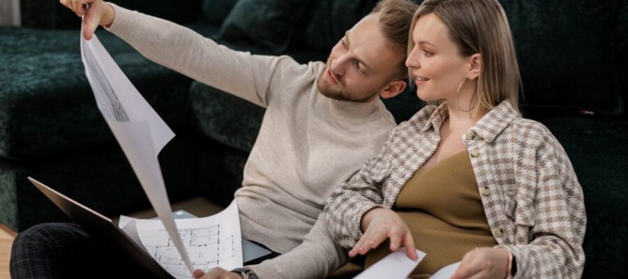 A couple sitting on a sofa reviewing architectural blueprints, symbolizing home buying or renovation.