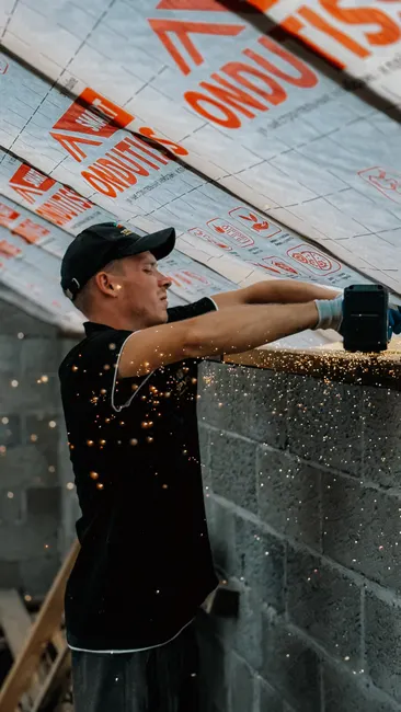 A focused construction worker cutting insulation boards on a roof with sparks flying.