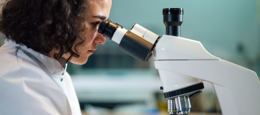 A focused scientist examines samples under a microscope in a laboratory setting.