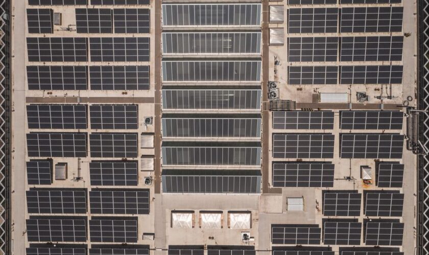 A high-angle drone shot capturing a grid of solar panels on a large industrial rooftop, showcasing renewable energy.