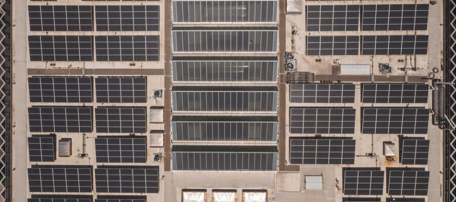A high-angle drone shot capturing a grid of solar panels on a large industrial rooftop, showcasing renewable energy.