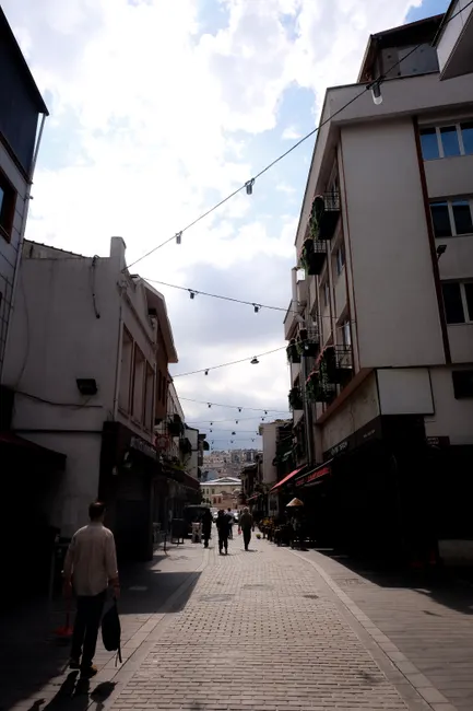 A lively narrow alley with string lights, showcasing urban architecture and pedestrians.