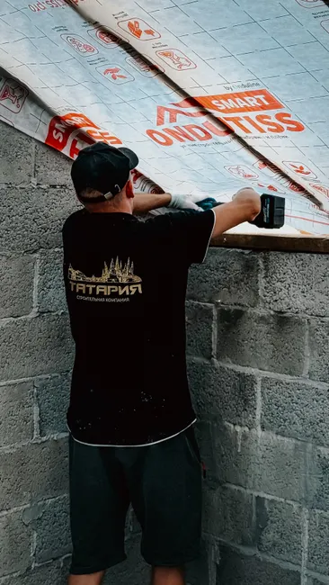 A man using a drill to install roofing insulation on a concrete building wall.