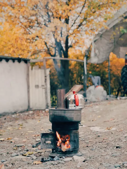 A rustic outdoor stove with a kettle boiling, surrounded by autumn foliage.