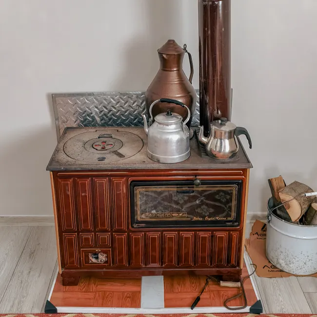 A rustic Turkish wood-burning stove with metal teapots and wood fuel, showcasing traditional cooking methods.