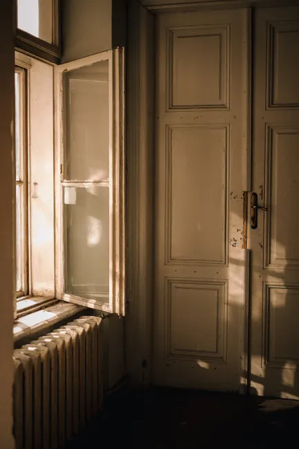 A serene interior scene with sunlight through an open window illuminating a classic door.