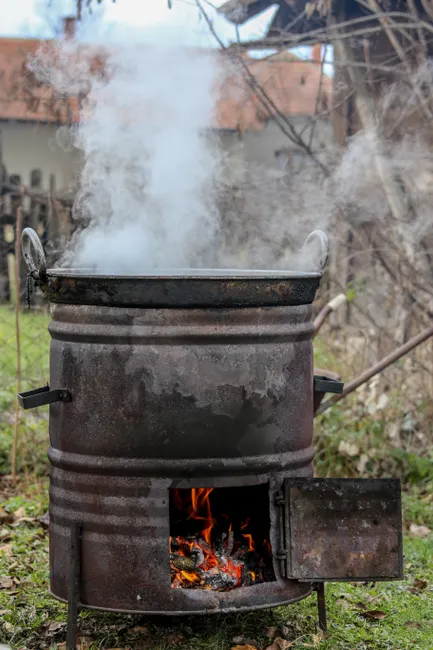 A steaming pot over a rustic wood stove outdoors emitting smoke and flames.