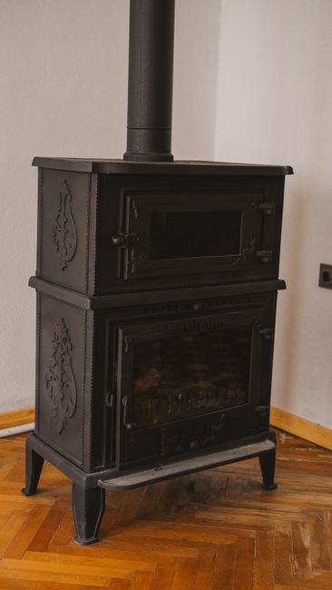 A vintage black iron wood stove in a cozy room with parquet flooring, exuding warmth and rustic charm.
