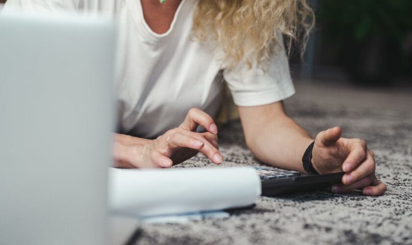 A woman engages in budget planning using a calculator on a comfortable carpeted floor.