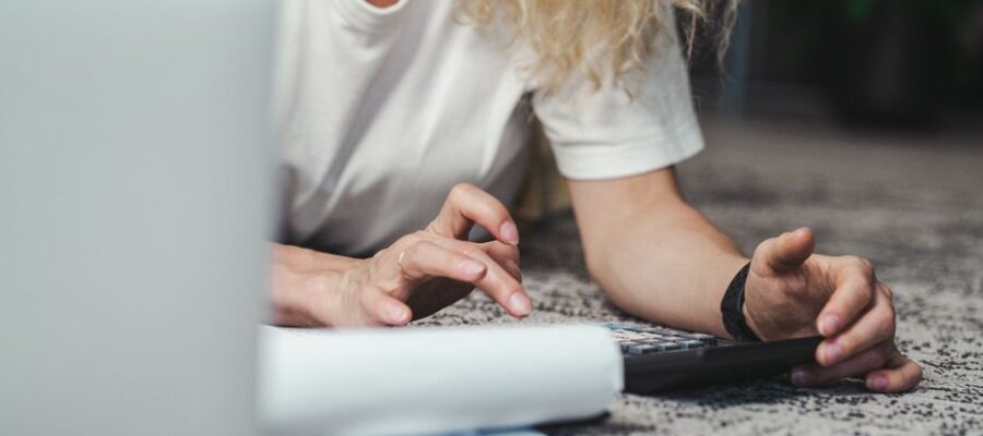 A woman engages in budget planning using a calculator on a comfortable carpeted floor.