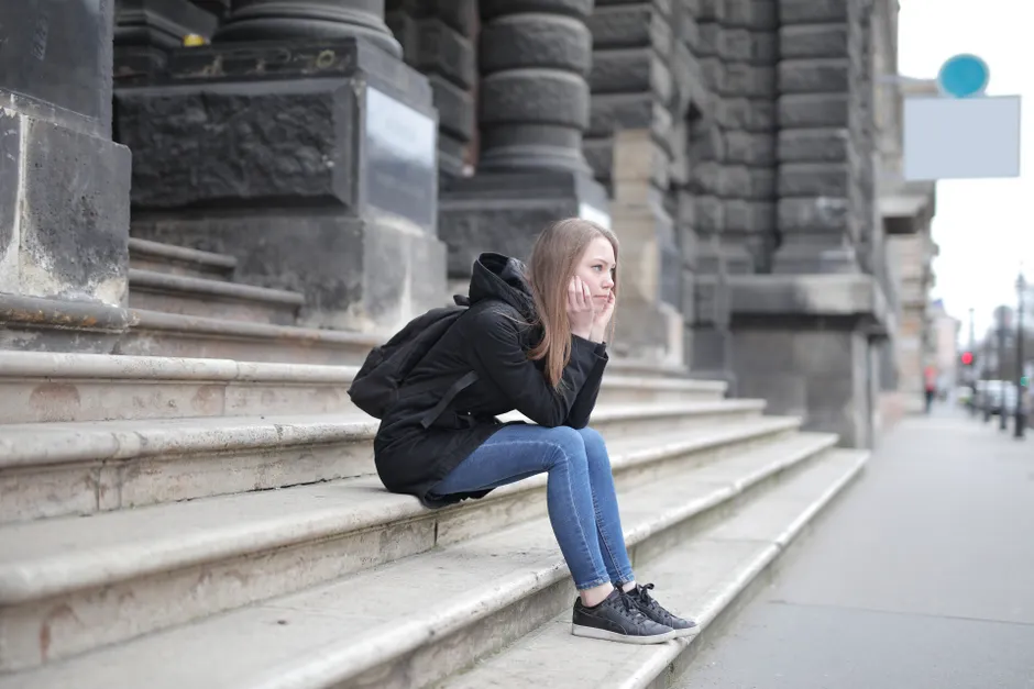 A young woman in casual wear sits alone on stone steps outside a historic building.