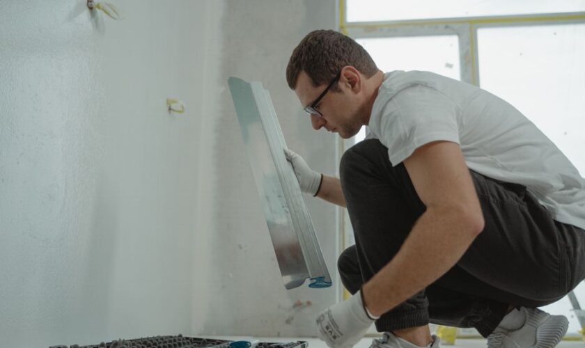 Adult male using metal trowel in interior home renovation project. White walls.