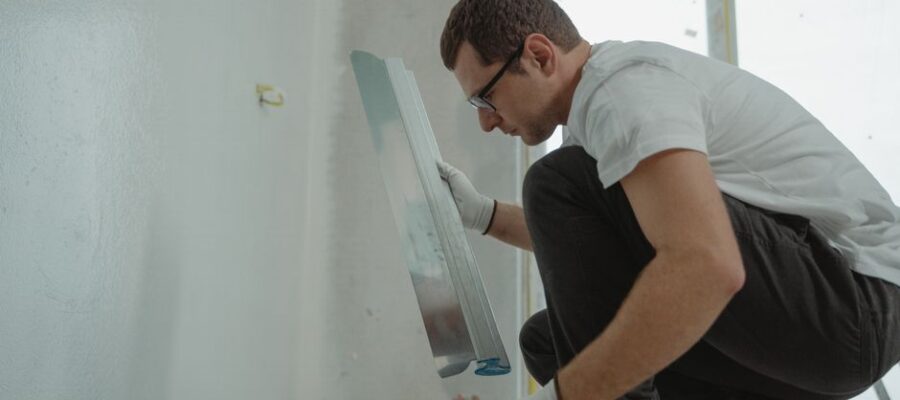 Adult male using metal trowel in interior home renovation project. White walls.