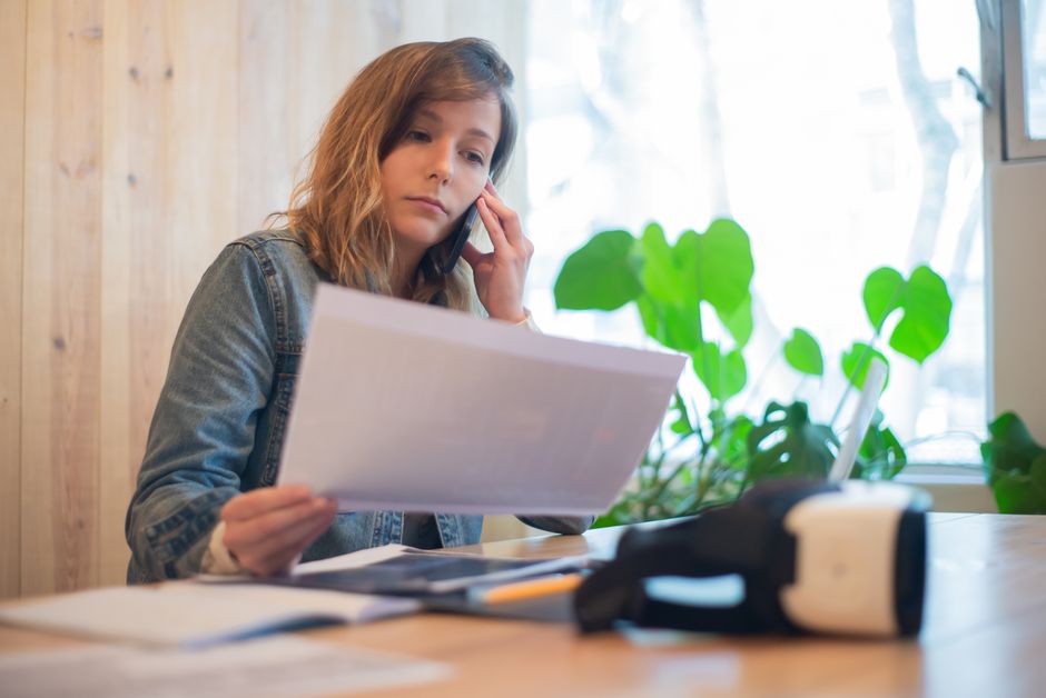 Businesswoman reviewing paperwork while on a call at a modern office workspace.