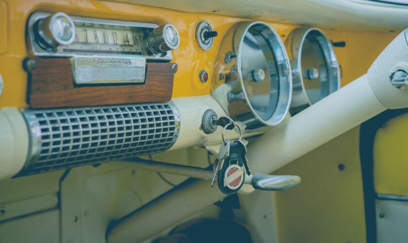 Close-up of a classic vintage car dashboard featuring an analog radio, speedometer, and keys.