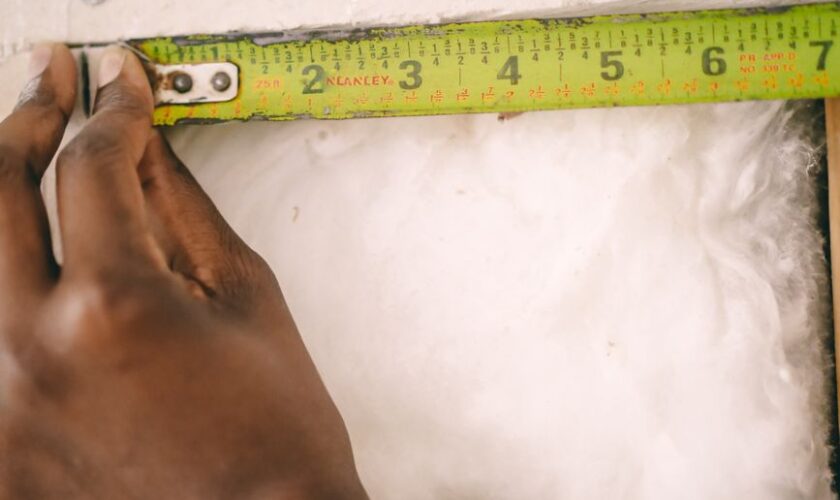 Close-up of a hand measuring insulation with a yellow tape measure.