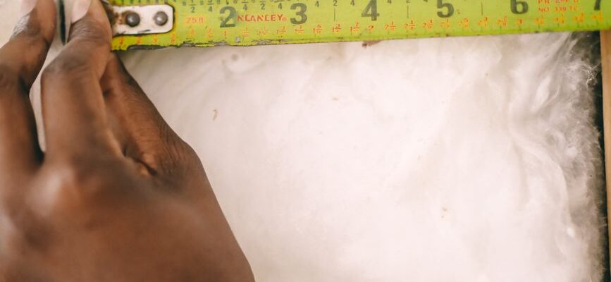 Close-up of a hand measuring insulation with a yellow tape measure.