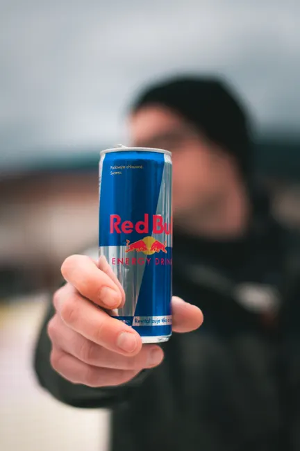 Close-up of a person holding a Red Bull energy drink can in a casual outdoor setting.