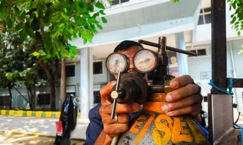 Close-up of a technician adjusting a gas regulator with pressure gauges in an outdoor setting in India.