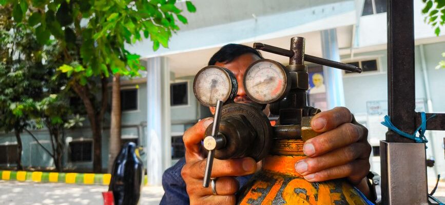 Close-up of a technician adjusting a gas regulator with pressure gauges in an outdoor setting in India.