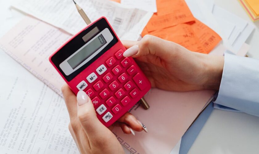 Close-up of hands holding a red calculator, managing finances with documents and receipts.