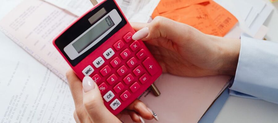 Close-up of hands holding a red calculator, managing finances with documents and receipts.