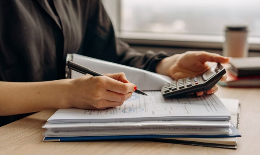 Close-up of person using a calculator with financial documents in an office.