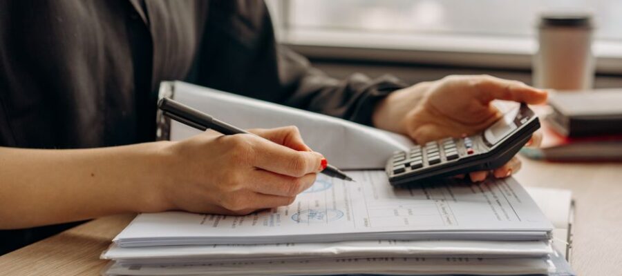Close-up of person using a calculator with financial documents in an office.