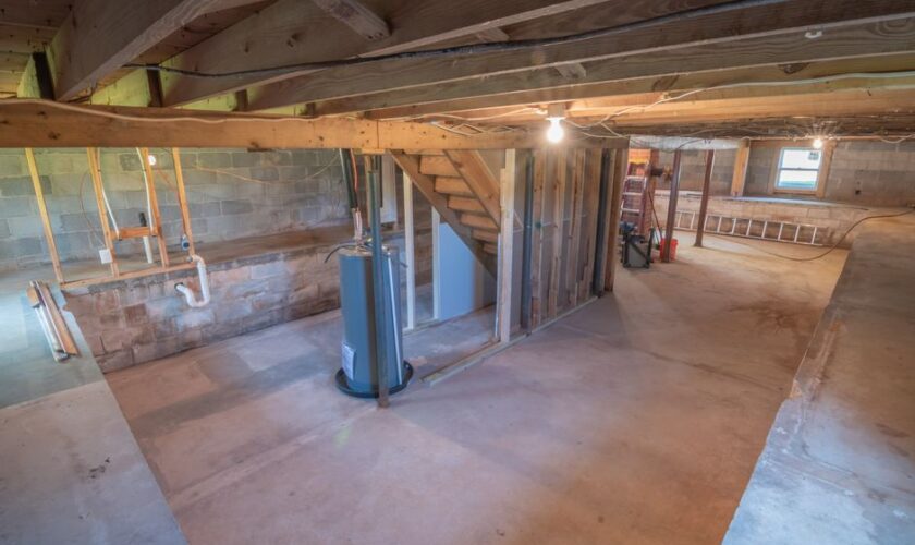 Empty basement with exposed beams and plumbing pipes, ideal for renovation.