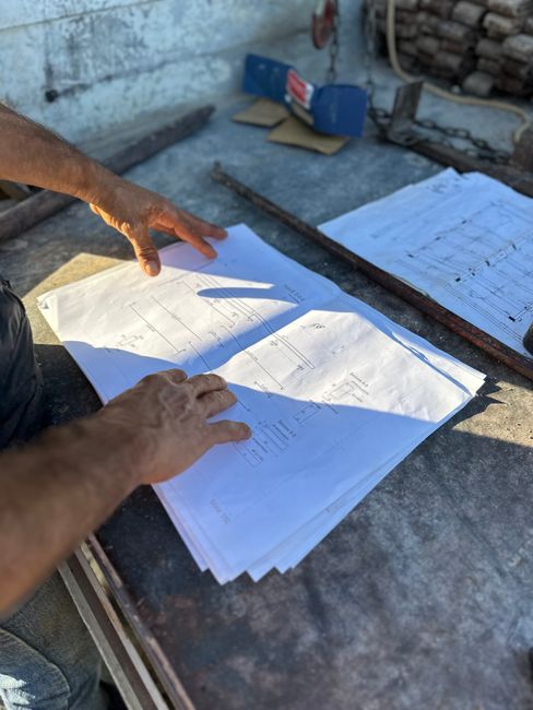 Hands examining construction blueprints on a table under sunlight in Montallegro, Sicily.