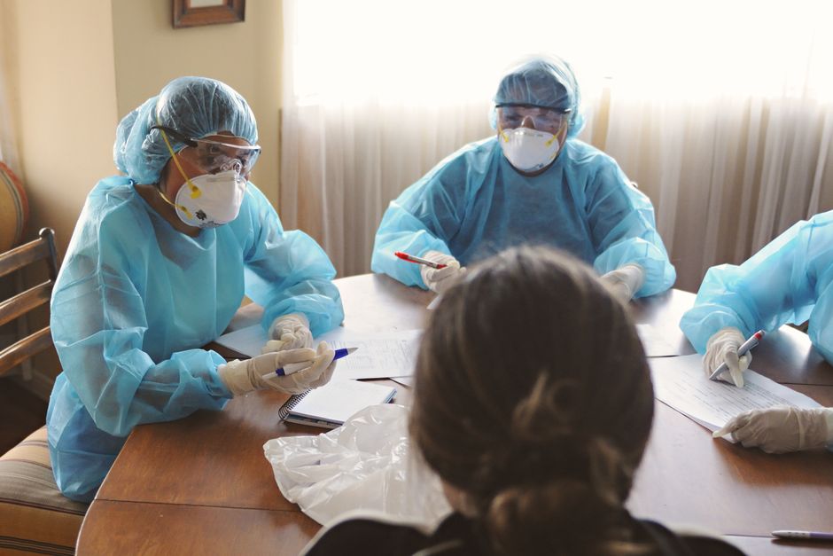 Healthcare professionals in PPE discuss operations during a meeting indoors.