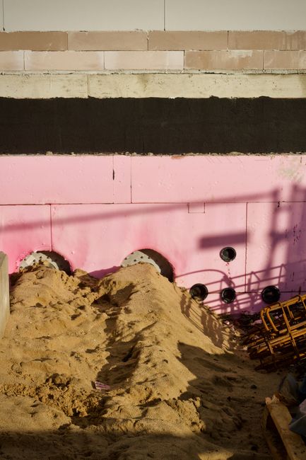 Image of a construction site featuring pink insulation panels against a sandy foreground.