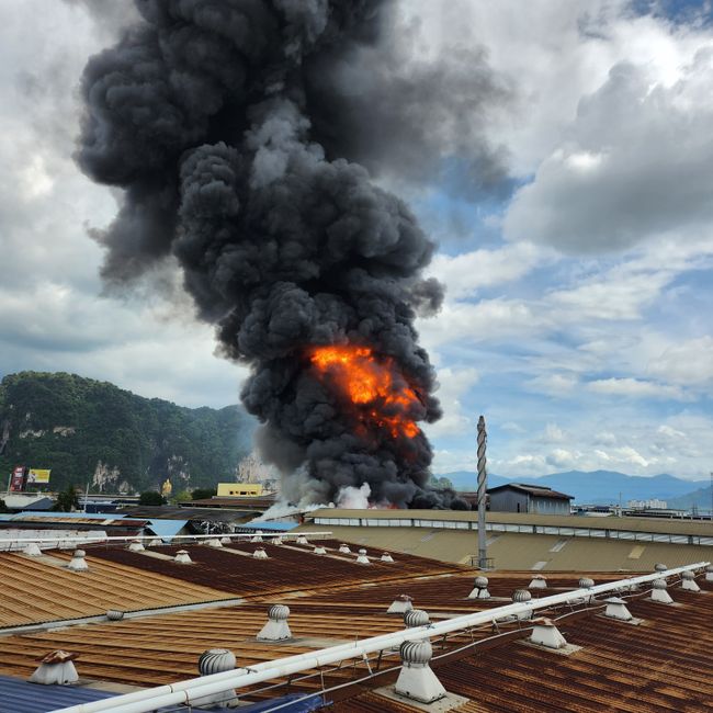 Intense factory fire causing thick black smoke and bright flames in an industrial district.