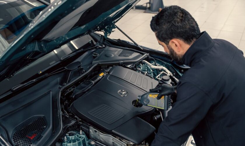 Mechanic inspecting and filling engine oil in a car at an indoor service center.