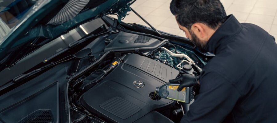 Mechanic inspecting and filling engine oil in a car at an indoor service center.