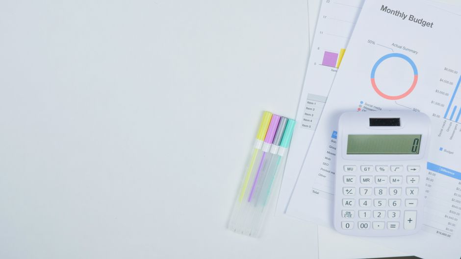 Minimalist office desk with a calculator, budget planning documents, and colorful pens.