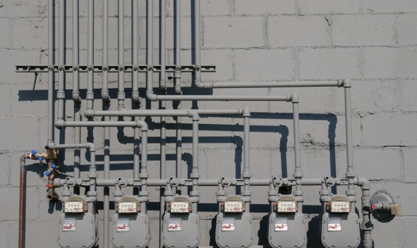 Row of gas meters and piping mounted on a concrete wall, illustrating urban utilities.
