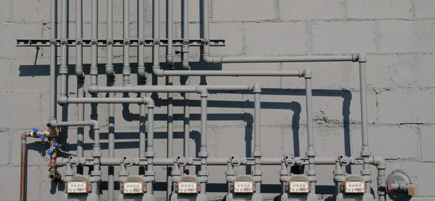 Row of gas meters and piping mounted on a concrete wall, illustrating urban utilities.