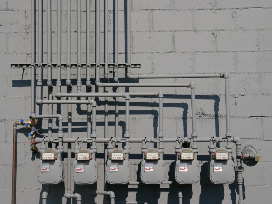 Row of gas meters and piping mounted on a concrete wall, illustrating urban utilities.