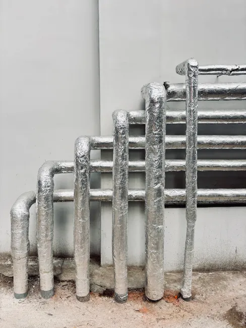 Silver insulated pipes arranged vertically on a building exterior, showcasing industrial architecture.