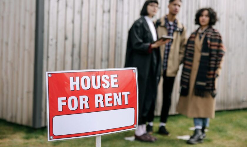 Three adults examining a house for rent sign outdoors, depicting diverse and inclusive interest in rental properties.