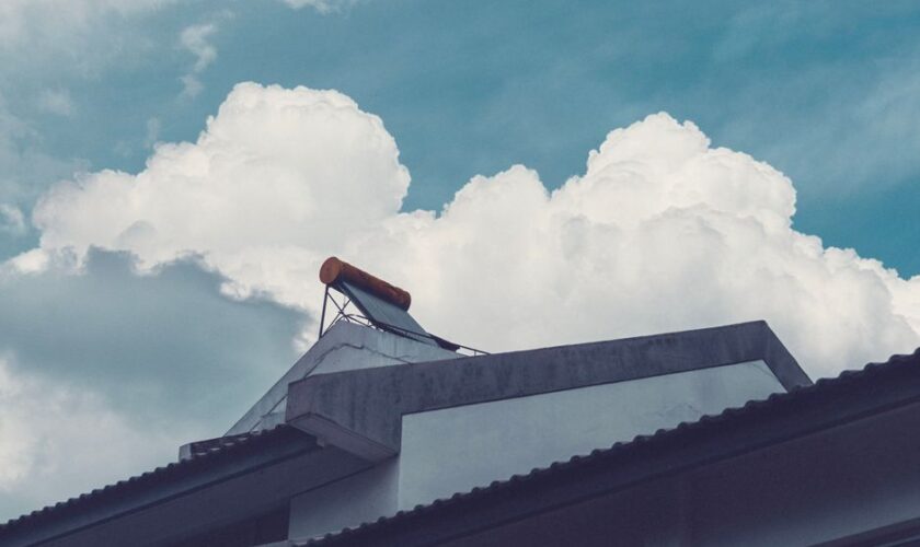 A building rooftop with a solar water heater set against a bright, cloud-filled sky.