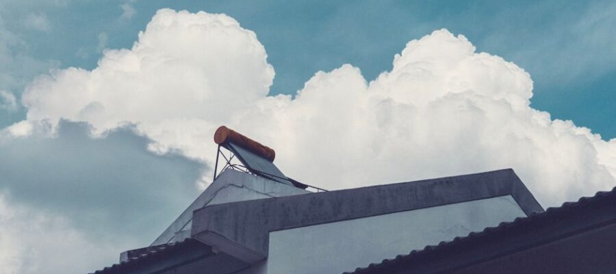 A building rooftop with a solar water heater set against a bright, cloud-filled sky.
